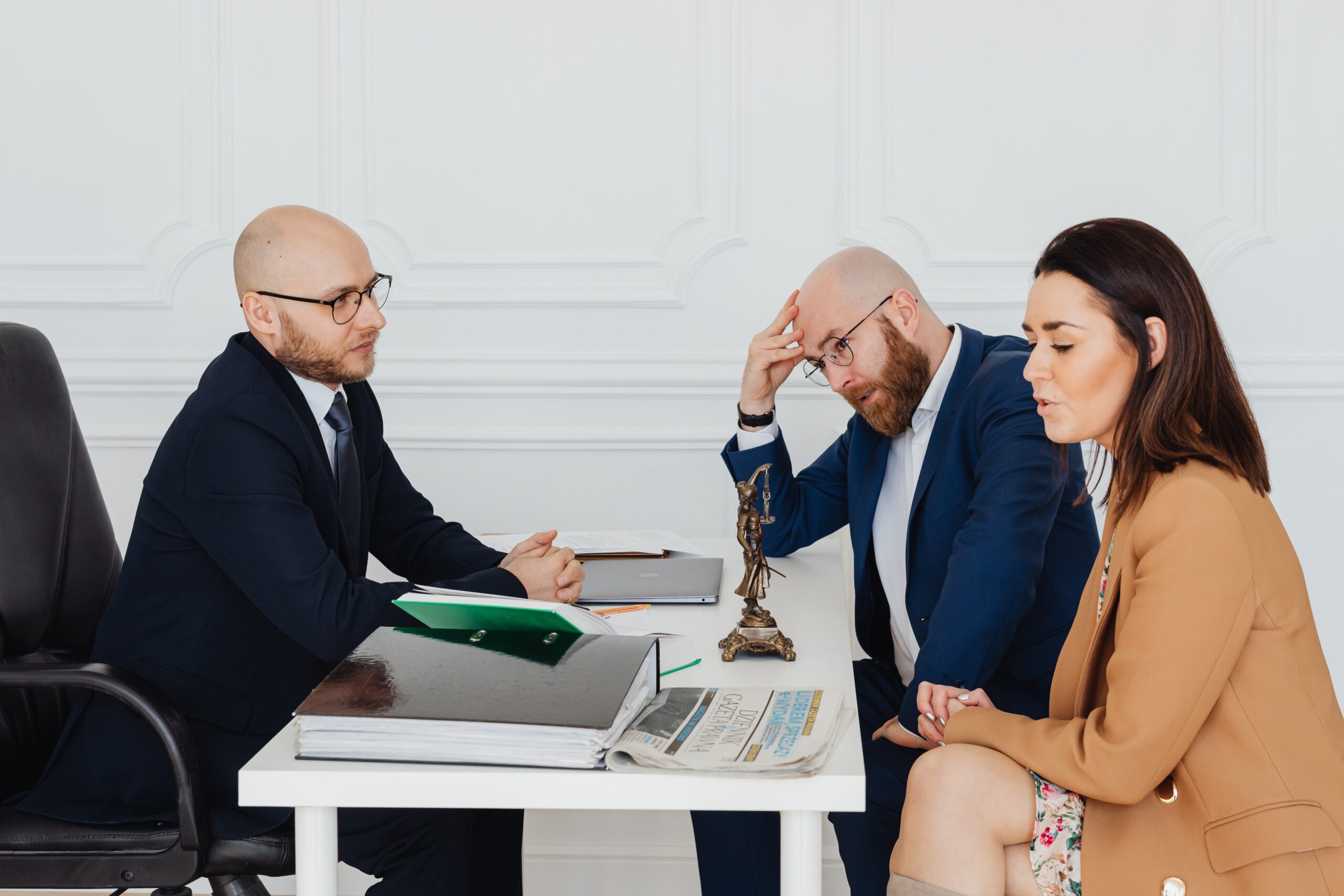 Distressed man and woman sit at a white desk with a male attorney.