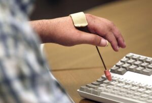 A hand outfitted with a simple assistive device for pressing keys on a computer keyboard.