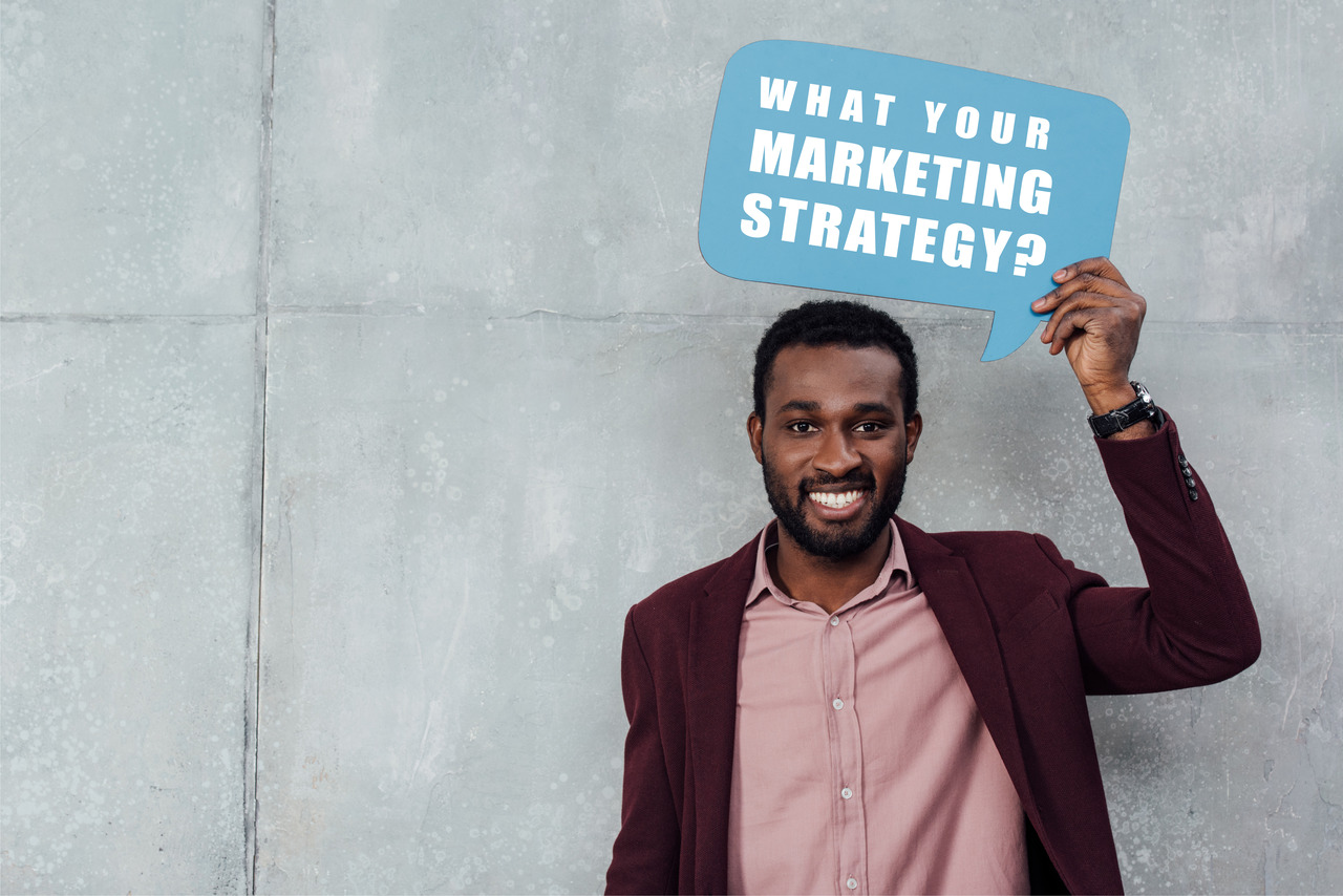 A man holding a sign that says "What Is Your Marketing Strategy?"